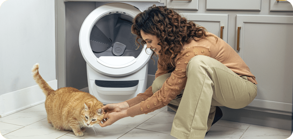 A woman petting an orange cat near a Litter-Robot 4.